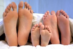 photo of three pairs of feet poking out of the bottom of the bed, child's feet in the middle